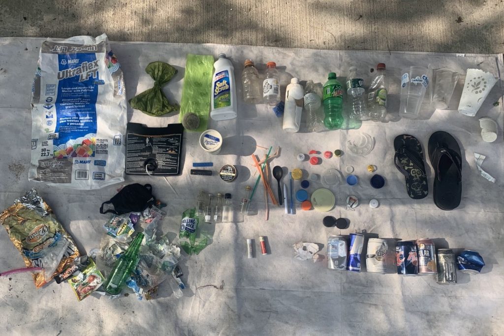 A variety of trash organized into categories on a white tarpaulin sheet